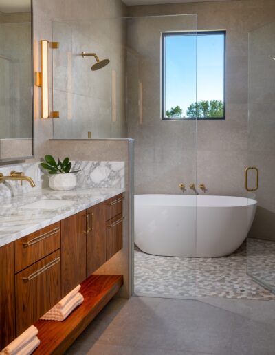 Modern bathroom with a marble countertop, wooden vanity, vessel tub, glass shower enclosure, wall-mounted fixtures, and a window providing natural light.